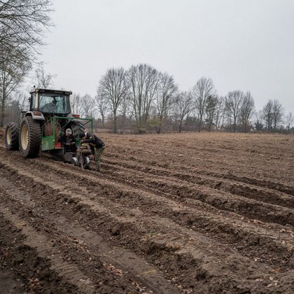 Sadzenie lasu - zaorane pole, w oddali ciągnik z naczepą służącą do sadzenia drzew.